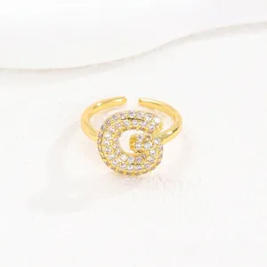 Detail van de fonkelende pavé-gezette letter G op een goudkleurige open ringband.