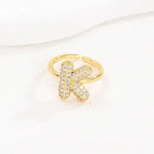 Detailweergave van een goudkleurige open ring met een sprankelende letter K bezet met zirkoon.