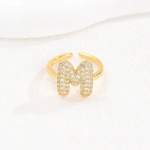 Gedetailleerde weergave van verstelbare gouden ring met letter M en sprankelend pavé