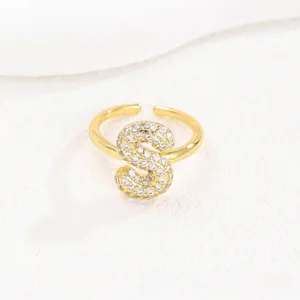 Close-up van een goudkleurige ring met de letter S en heldere zirkonia-stenen