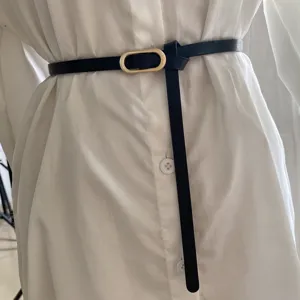 Close-up of minimalist black thin leather belt with elegant gold oval buckle for women detail.