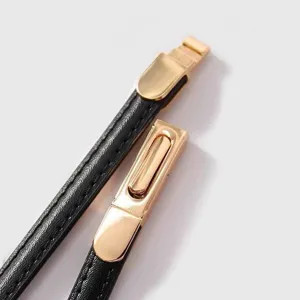 Detailed shot of a thin black leather women's belt with a stylish gold metal clasp buckle.