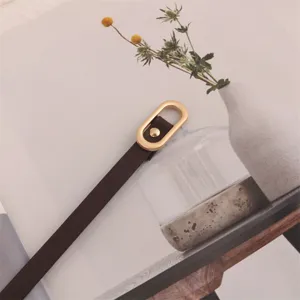 Close-up detail of a women's slim dark brown leather belt featuring a chic gold oval metal buckle.