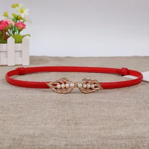 Detail shot of red leather thin belt with golden leaf pearl buckle, elegant accessory closeup.