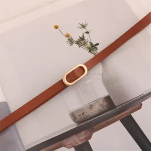 Minimalist women narrow leather belt with oval metal buckle detail, stylish accessory.