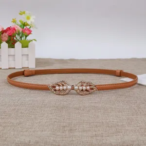 Detail view of a slim brown leather belt featuring a chic gold leaf pearl snap buckle.