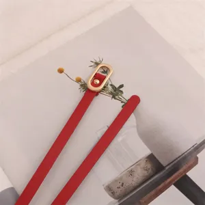 Close-up detail of a red slim leather belt featuring a stylish gold-tone oval buckle.