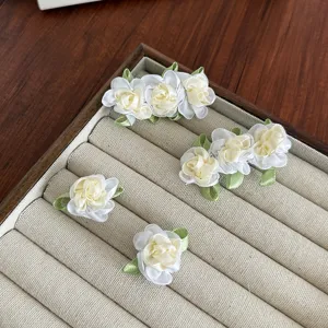 Elegante camelia bloem haarclips met groene bladeren op een houten sieradendisplay