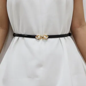 Close-up van dunne zwarte lakleren riem met elegante gouden parelgesp gedragen op witte jurk.