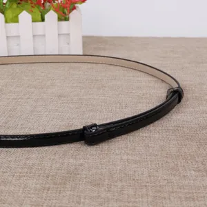 Gedetailleerd detail van een slanke zwarte laklederen riem op jute, perfect voor jurken.