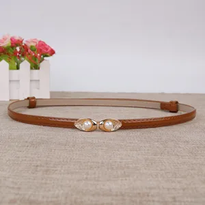 Detail van bruine smalle lederen riem met elegante gouden gesp en parelversiering.