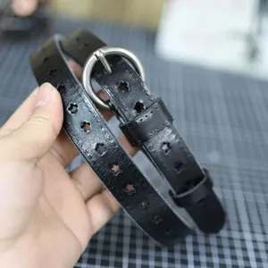 Black leather belt detail with star hollow design and silver metal round buckle closeup