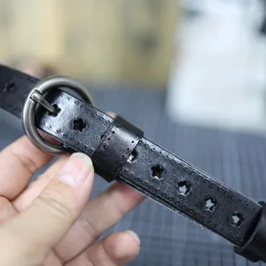 Detailed view of black leather belt with star hollow-out design and round metal buckle close up