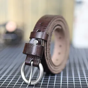 Detailed close-up of a brown genuine leather women belt with metal buckle on workshop mat.