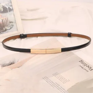 Détail d'une ceinture fine en cuir verni noir avec boucle rectangulaire dorée