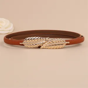 Close-up of thin brown leather belt featuring a chic double leaf golden metal buckle detail.