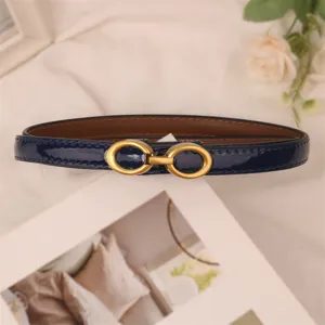 Dark blue patent leather thin women belt with gold double ring buckle detail close up view.