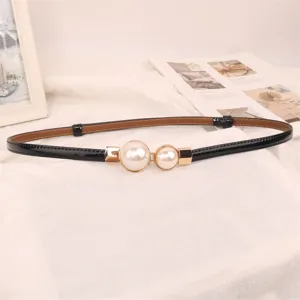 Detail view of a thin black patent leather belt with elegant double pearl gold buckle
