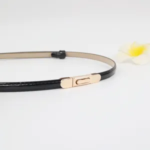 Close-up van een smalle zwarte laklederen riem met een subtiele gouden metalen gespsluiting.