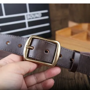 Detail shot of dark brown genuine leather men's belt with vintage brass pin buckle for trousers.