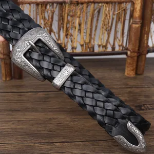 Close-up detail of a vintage black woven leather belt featuring an ornate silver buckle