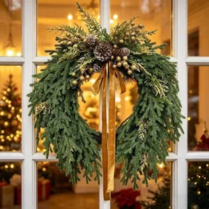 Festive Norfolk pine Christmas wreath with a velvet bow hanging on a white window frame.