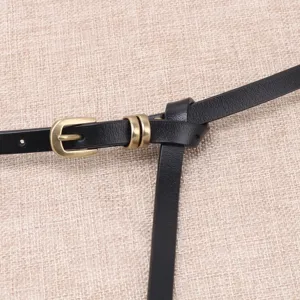 Primer plano detallado del cinturón de cuero negro fino con hebilla de bronce y nudo elegante.