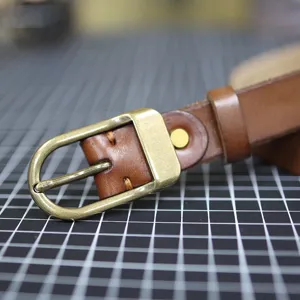 Close-up of brown leather belt with retro brass buckle, showing fine stitching details.