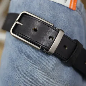 Primo piano dettagliato di una cintura da uomo in vera pelle con fibbia metallica sui jeans.