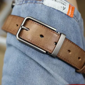 Dettaglio in primo piano di cintura da uomo in vera pelle vintage indossata su jeans.