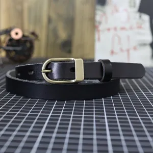 Close-up detail of black leather belt with vintage brass buckle on grid workspace background.