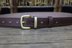 Close-up of vintage brown leather belt with brass pin buckle and fine stitching details.
