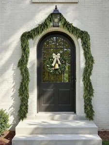 Detailed view of lush green Norfolk pine garland decorating a white brick archway and black door.