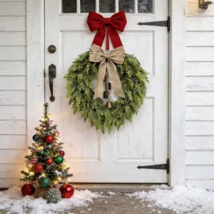 Couronne de Noël en cèdre avec nœud en toile et cloches sur porte d'entrée blanche