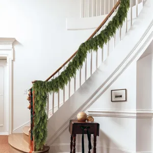 A realistic green Norfolk pine garland draped elegantly over a classic white staircase.