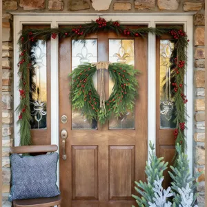 Norfolk pine wreath with red berries and garland hanging on a wooden front door.
