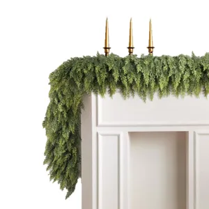 Realistic green Norfolk pine garland draped over a white fireplace mantel with gold candles.