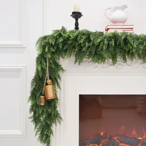 Artificial Norfolk pine garland draped on white fireplace with decorative bells