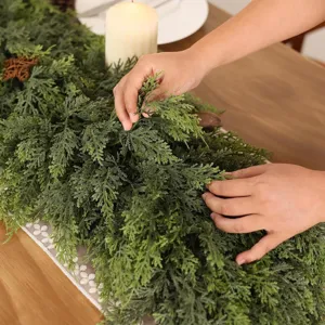 Close-up of hands arranging a realistic Norfolk pine garland on a wooden table.
