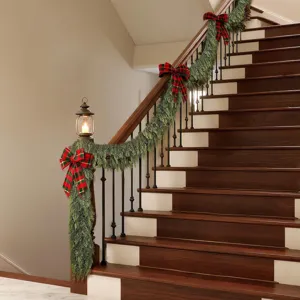Realistic Norfolk pine Christmas garland with red plaid bows draped on a staircase