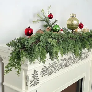 Vista detallada de guirnalda de cedro navideño con bolas de colores en una repisa de chimenea.