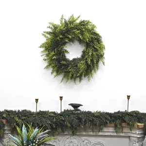Lush green cedar wreath and matching garland displayed on a white wall and fireplace.