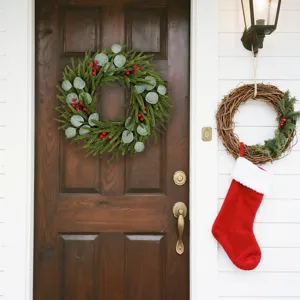 Festive Christmas wreath with pine needles and red berries on a rustic wooden front door.