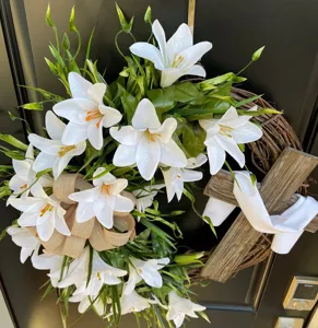 Detailed view of an Easter cross wreath with white lilies and burlap bow on a black door