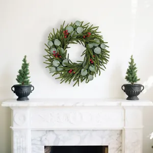 Lush Christmas wreath featuring cypress, eucalyptus, and red berries on a clean white wall.