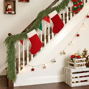 Realistic Norfolk pine garland on a white staircase with festive red knitted stockings