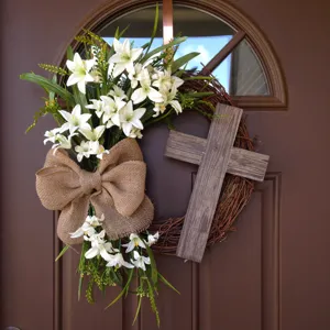 Detailed view of an Easter wreath with white lilies and a wooden cross on a brown door.