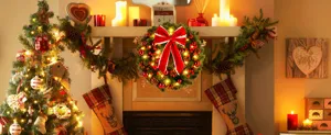 Macro view of festive Christmas wreath with red bow and warm LED lights on a fireplace mantel.