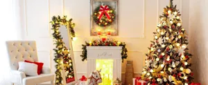 Illuminated Christmas wreath with a large red bow hanging above a white fireplace mantel