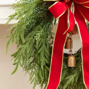 Close-up detail of a lush Christmas wreath featuring a large red bow and copper bells